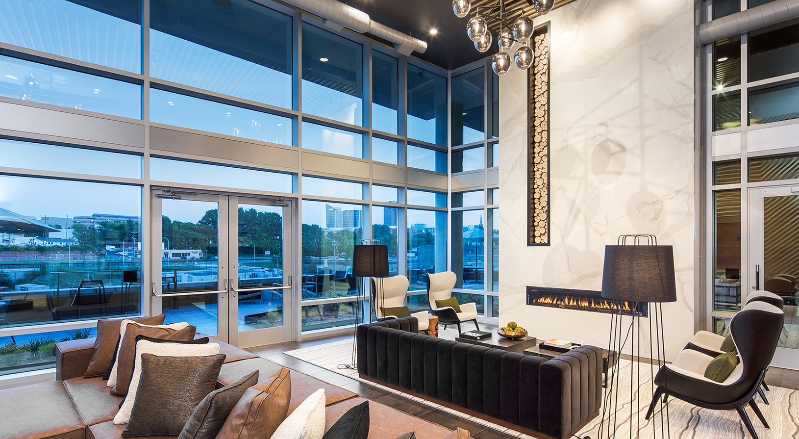 Peace Raleigh Apartments clubroom with large fireplace and wall to wall windows with a view of the city at sundown