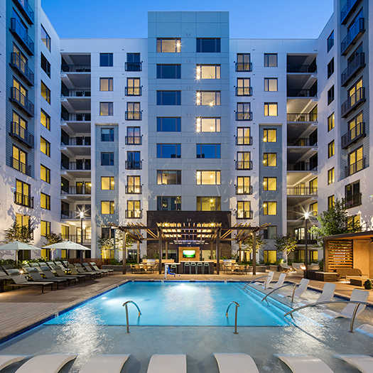Peace Raleigh Apartments pool in the courtyard with in-pool seating options and the building lit up at sundown